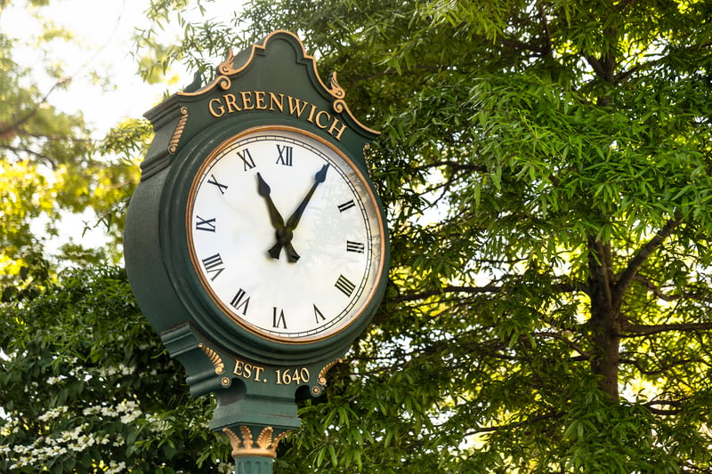The green street clock in downtown Greenwich, Fairfield County, Connecticut, framed by trees.