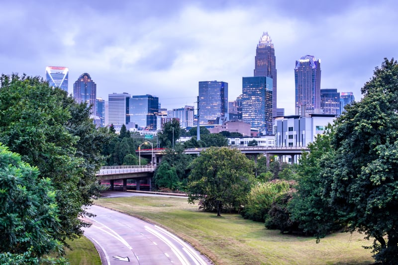 Charlotte, North Carolina, skyline above a tree-lined highway with evening traffic trails.