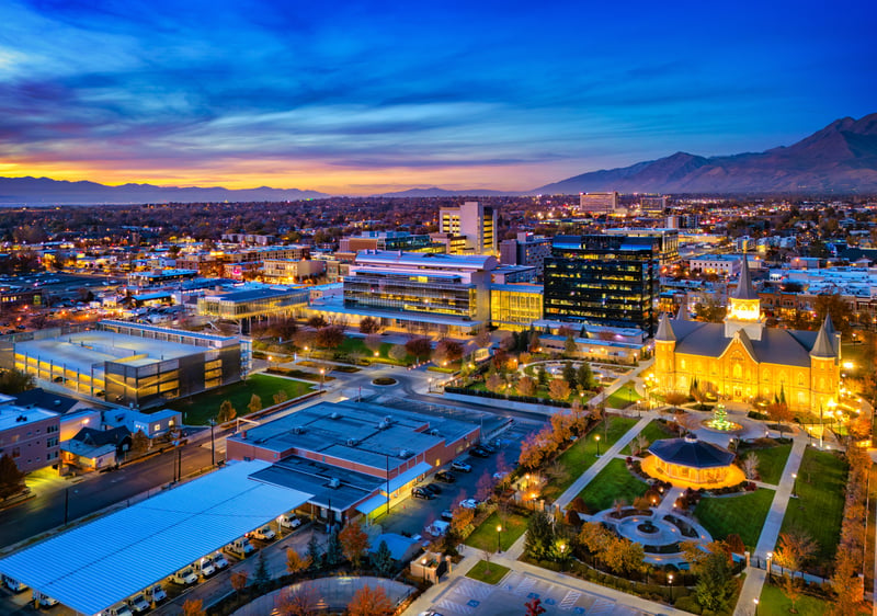 Downtown Provo, Utah, at dusk, with autumn trees and mountains in the distance.