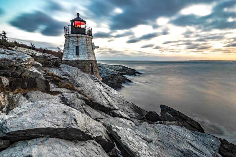 Castle Hill Lighthouse on the rocky shore of Newport, Rhode Island, at sunset.