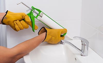 Sealant is applied between a wall and sink with a caulk gun.