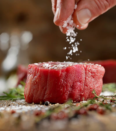 Flaky salt is used to season a filet mignon steak.