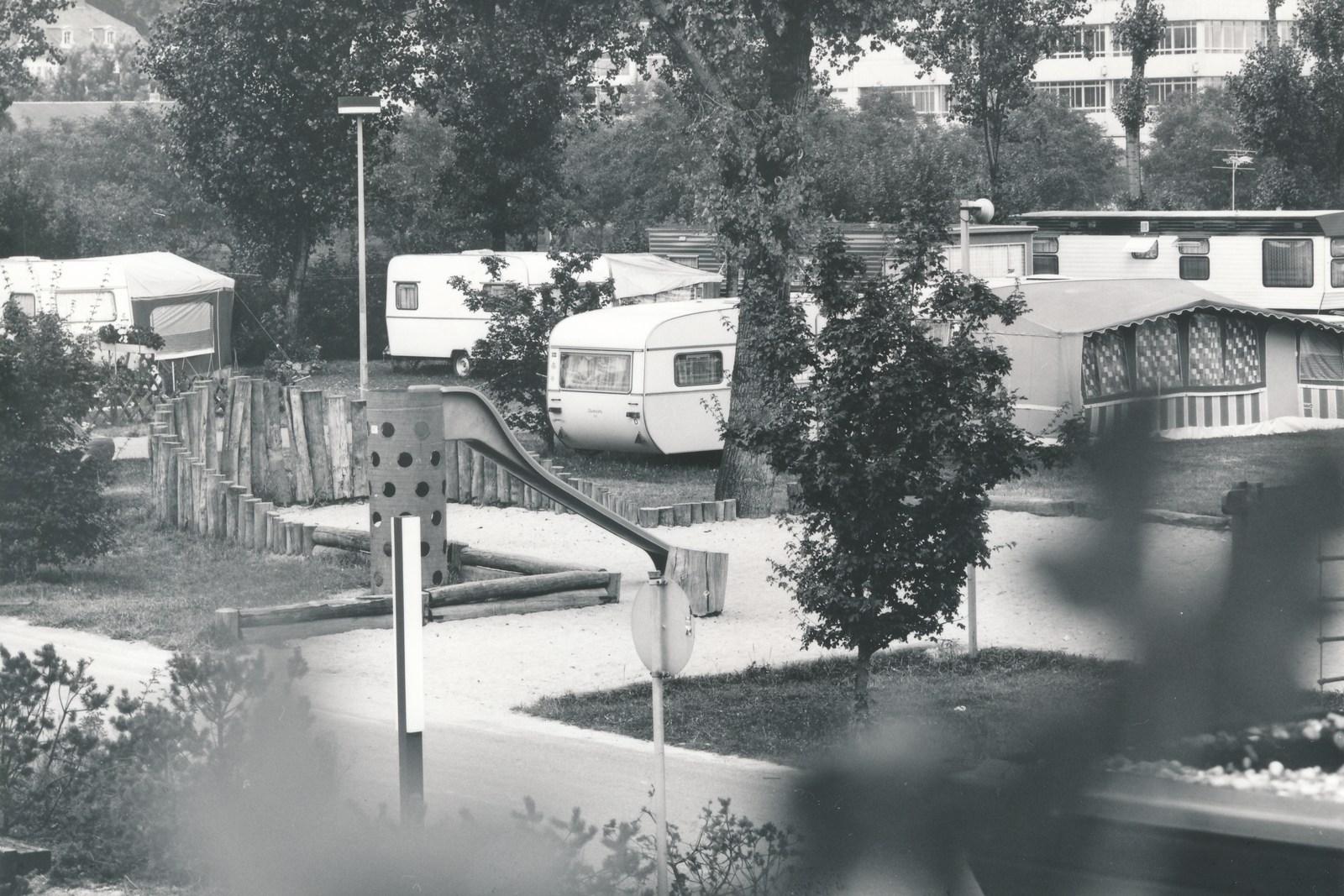 Caravans achter een houten hek op de vroegere camping, op de achtergrond een woongebouw