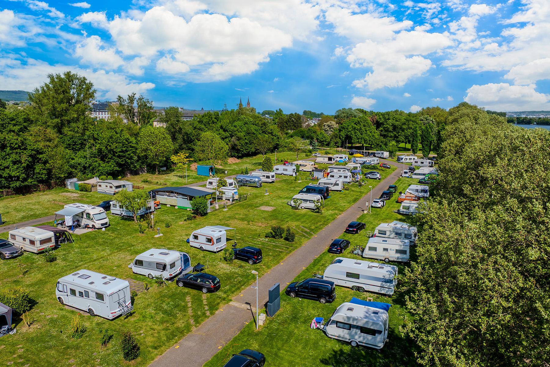 Luftfoto af Rheingaucamping Geisenheim – dronebillede af de rummelige pladser med autocampere, campingvogne og telte, omgivet af grønne arealer med Rhinen i baggrunden