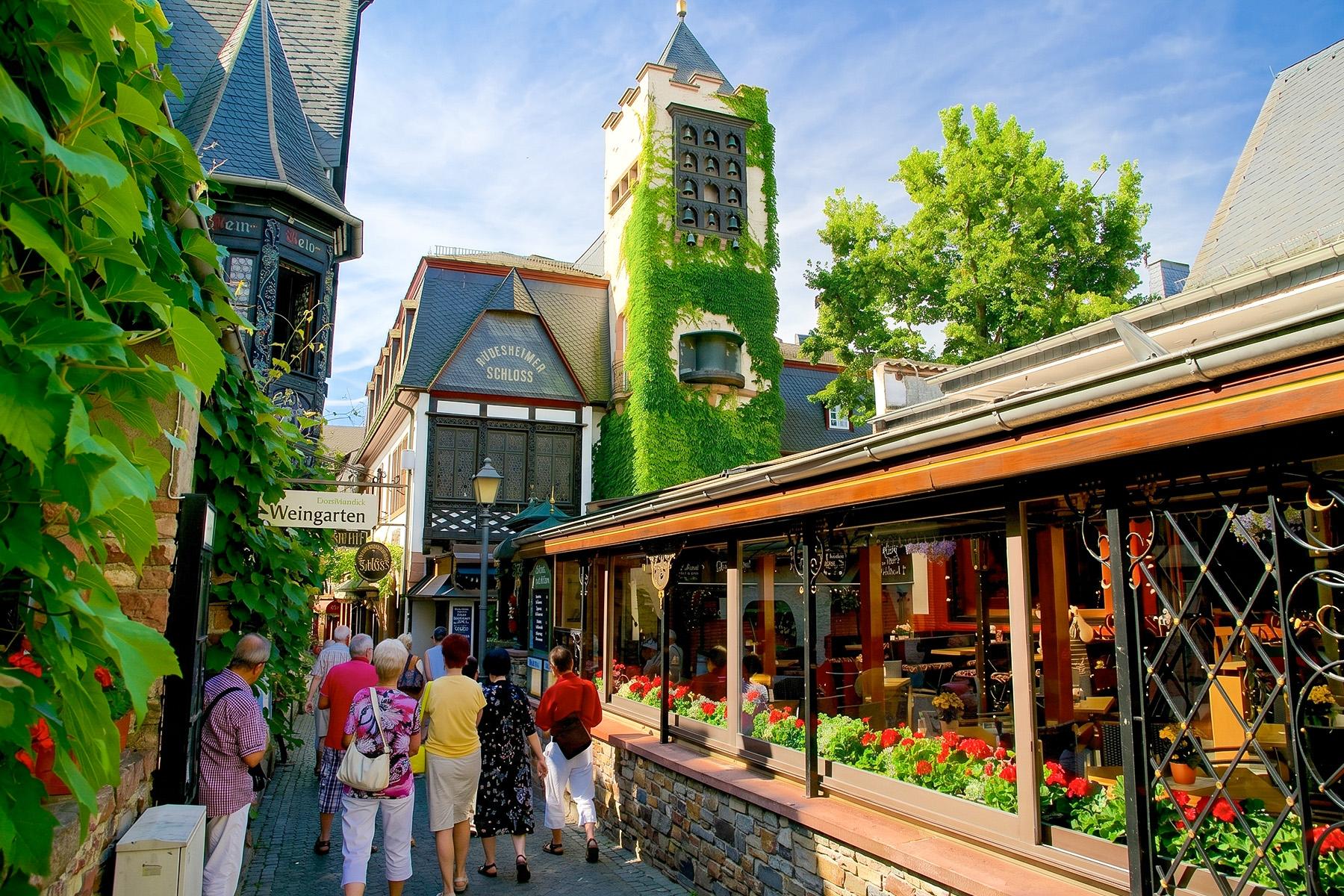 Drosselgasse Rüdesheim am Rhein – besøgende slentrer gennem den berømte vingasse med efeubegroet tårn og blomstrende restaurantterrasser i Rheingau