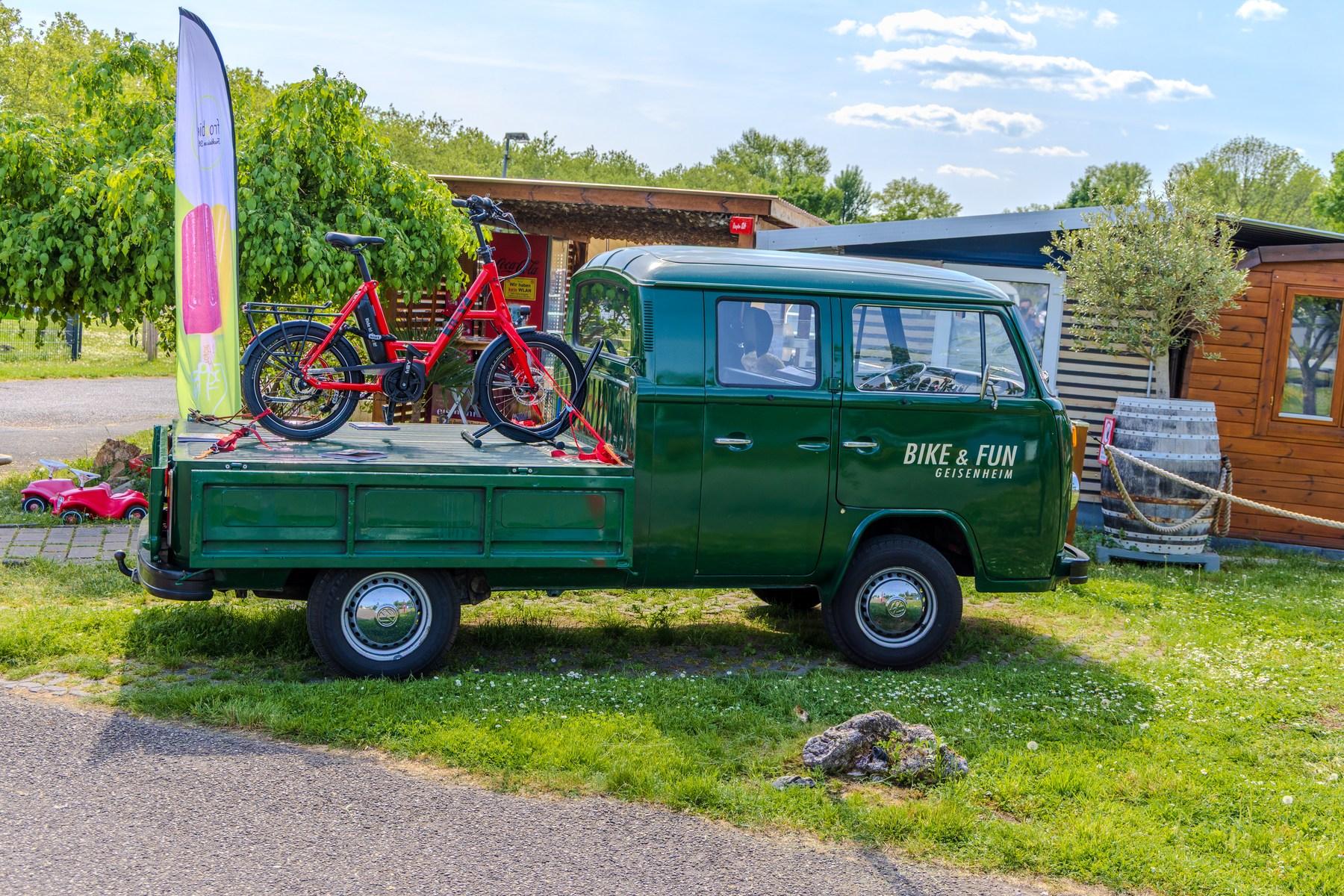 Grön VW-veteranpickup med hyrcyklar från Bike & Fun Geisenheim, med en tunnstuga bakom