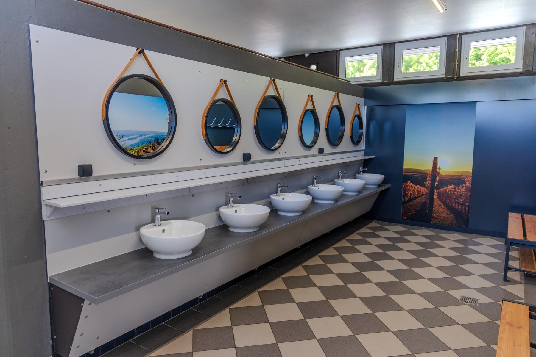 Rad med tvättplatser med bänkskålar och runda speglar i sanitetsbyggnaden på Rheingaucamping